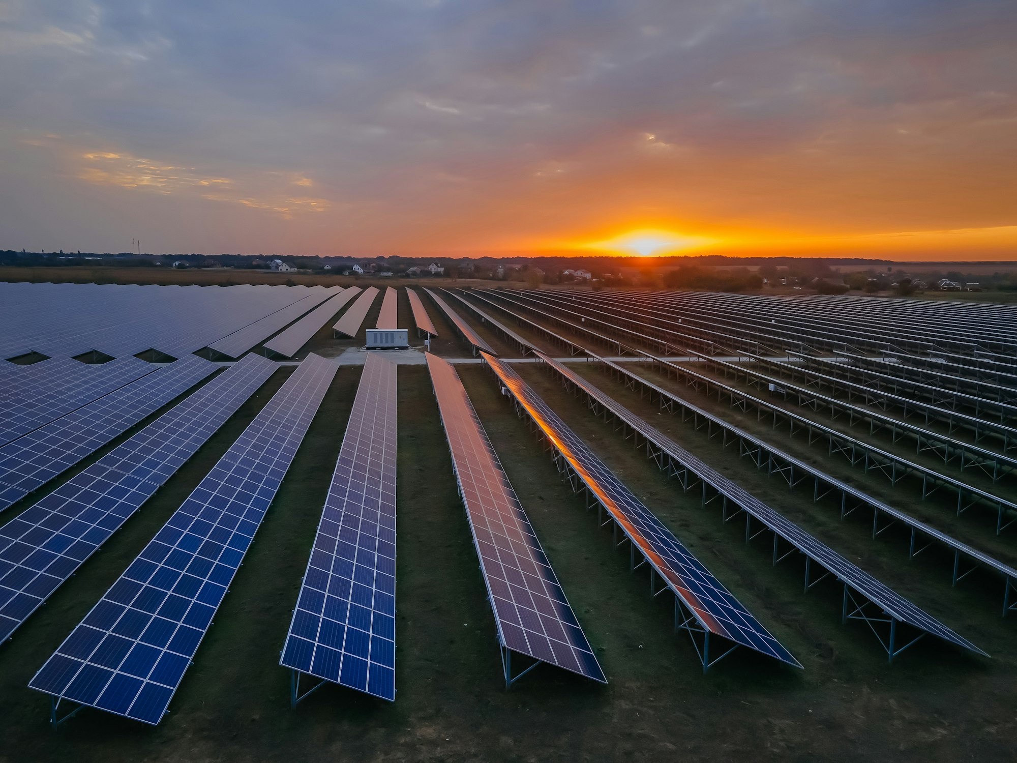 Aerial drone view into large solar panels at a solar farm at bright sunset. Solar cell power plants.